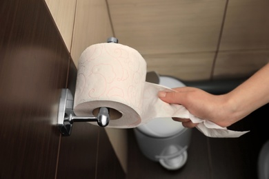 Photo of Woman pulling toilet paper from holder in bathroom