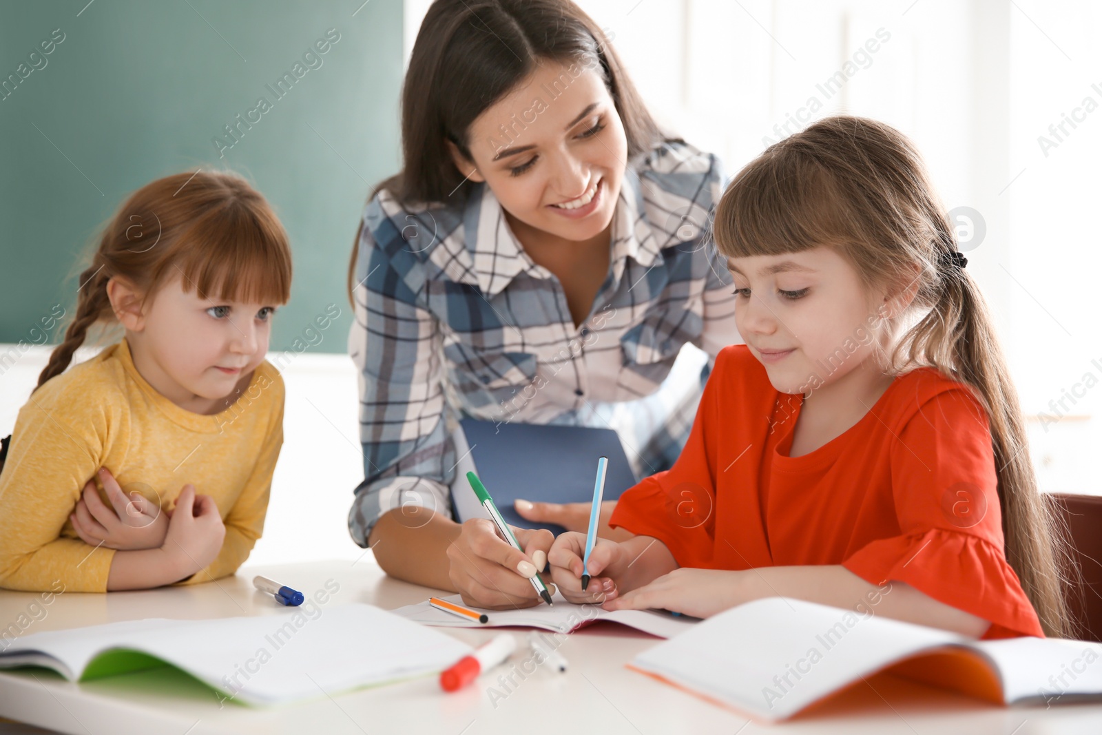 Photo of Female teacher helping girl with her task in classroom at school