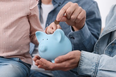 Photo of Family budget. Little girl and her parents putting coins into piggy bank, closeup