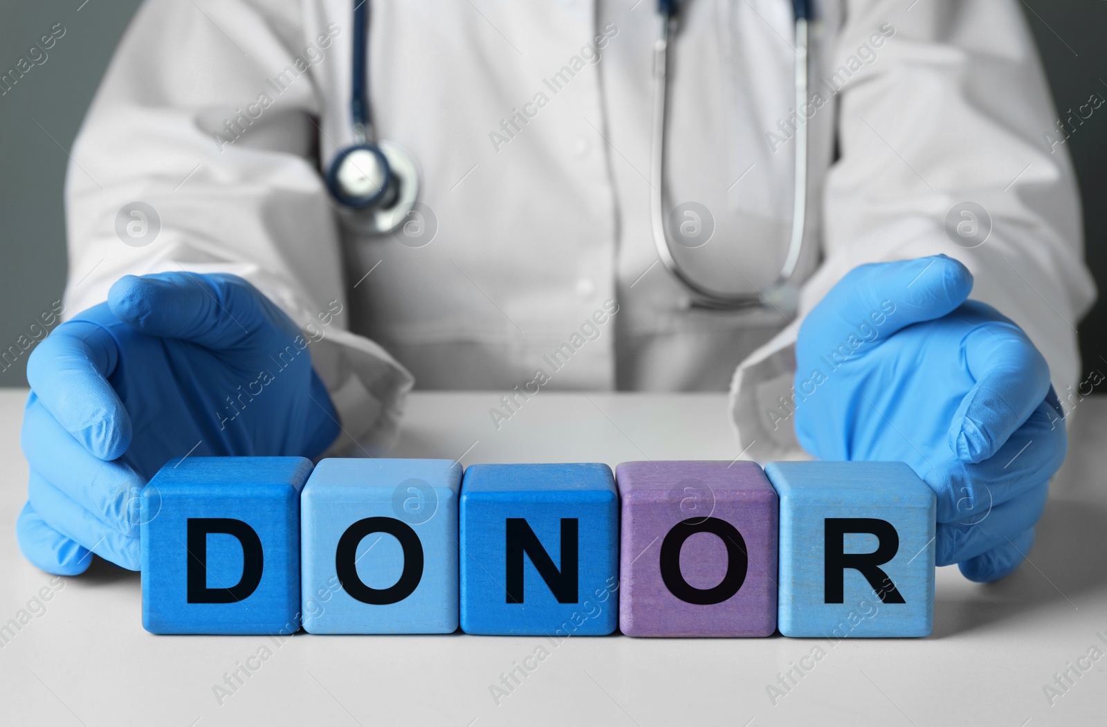 Photo of Doctor making word Donor of wooden cubes with letters at white table, closeup