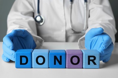 Photo of Doctor making word Donor of wooden cubes with letters at white table, closeup