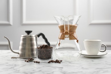 Photo of Glass chemex coffeemaker, kettle, beans in bowl and cup on white marble table