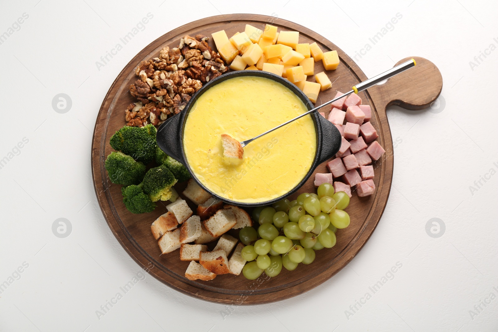 Photo of Fondue with tasty melted cheese, fork and different products on white table, top view