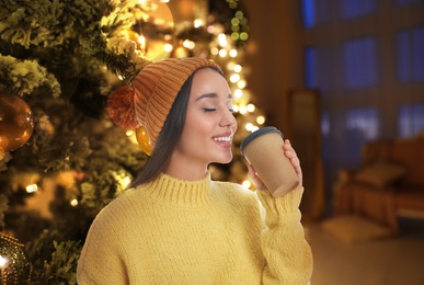 Happy beautiful woman with mulled near Christmas tree indoors