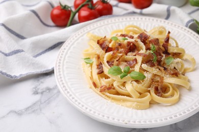 Tasty pasta with bacon and basil on white marble table, space for text