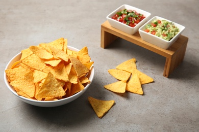 Photo of Bowl of delicious mexican nachos chips served with sauces on grey table