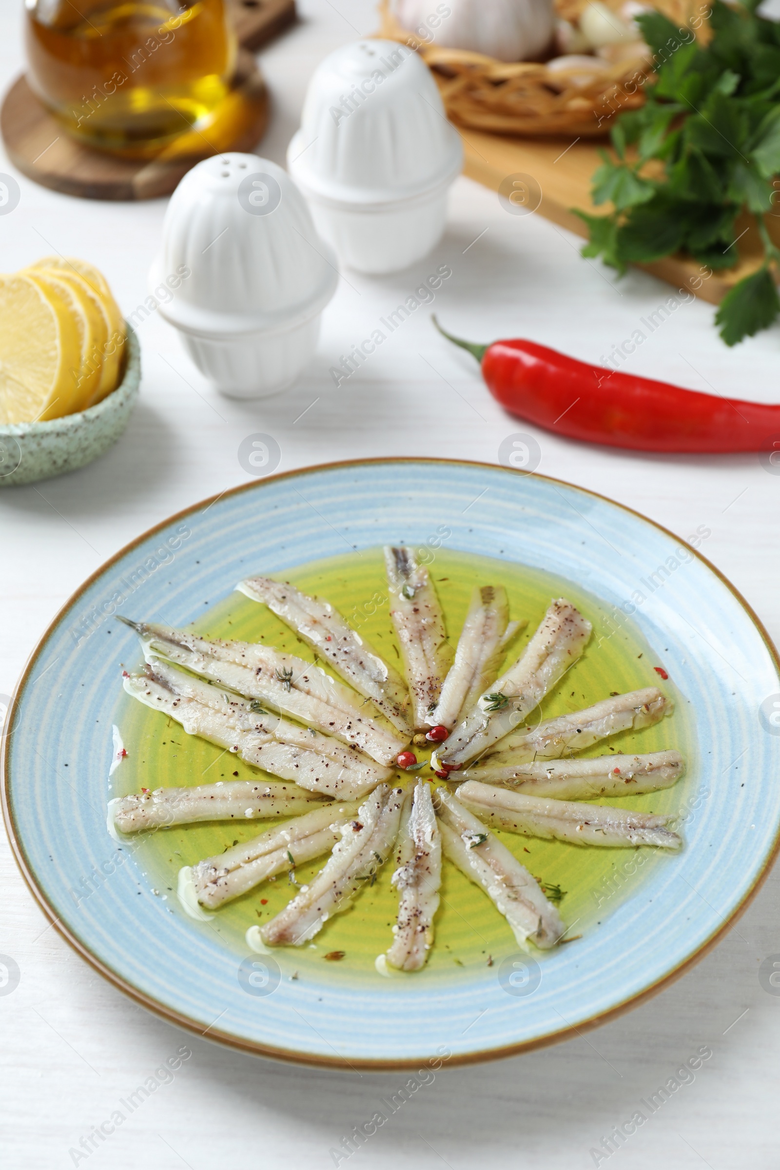 Photo of Tasty pickled anchovies with spices and products on white wooden table