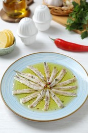 Photo of Tasty pickled anchovies with spices and products on white wooden table