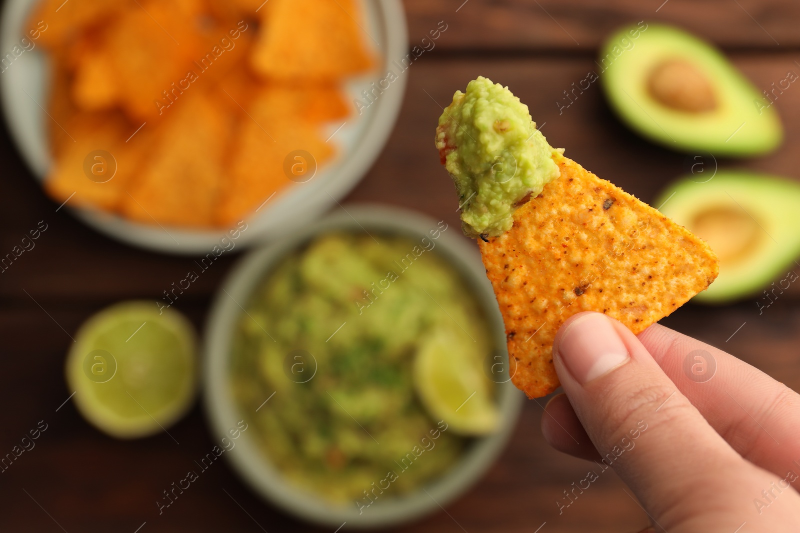 Photo of Woman holding delicious nachos chip with guacamole at wooden table, closeup. Space for text
