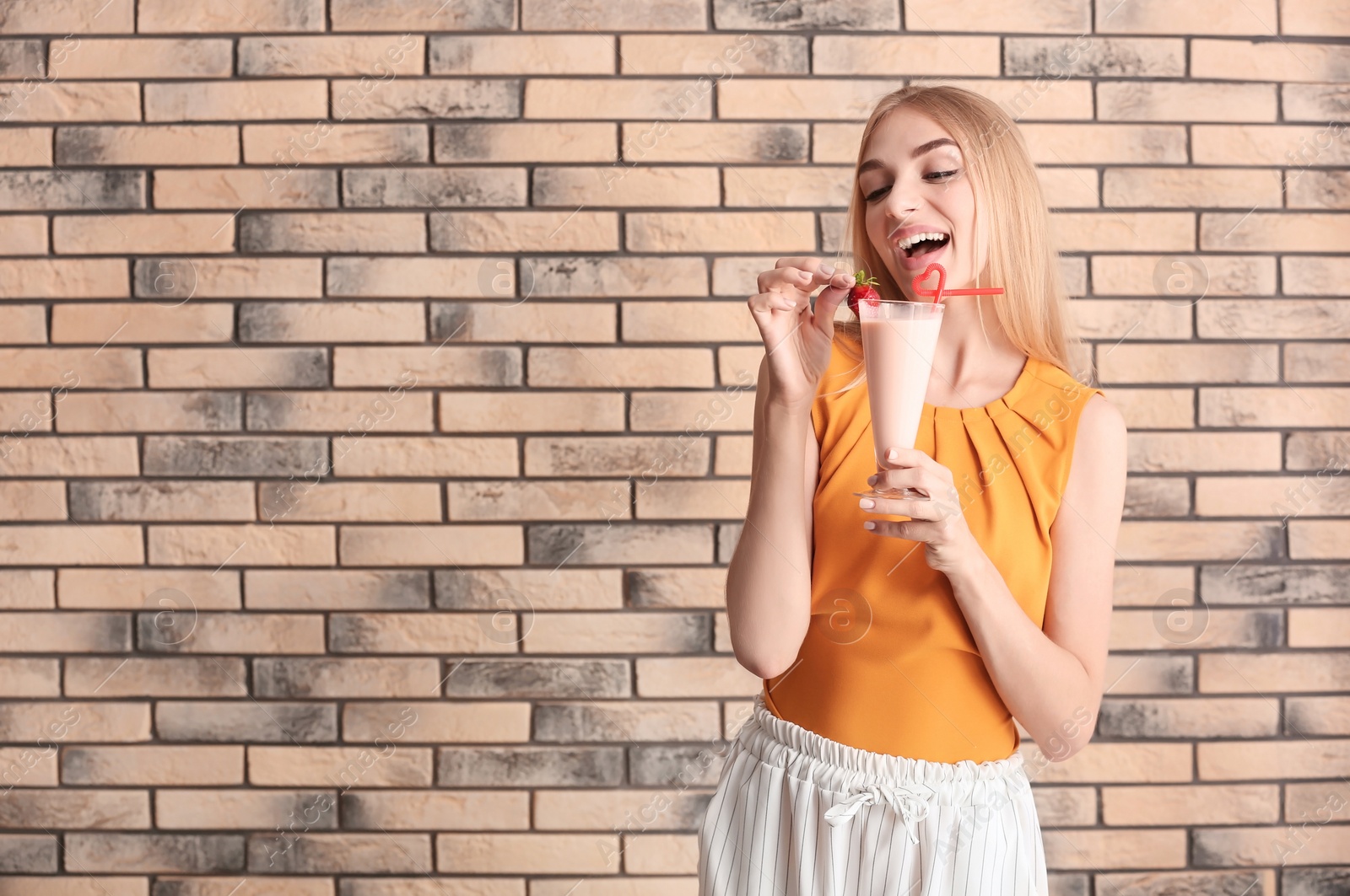 Photo of Young woman with glass of delicious milk shake on brick wall background