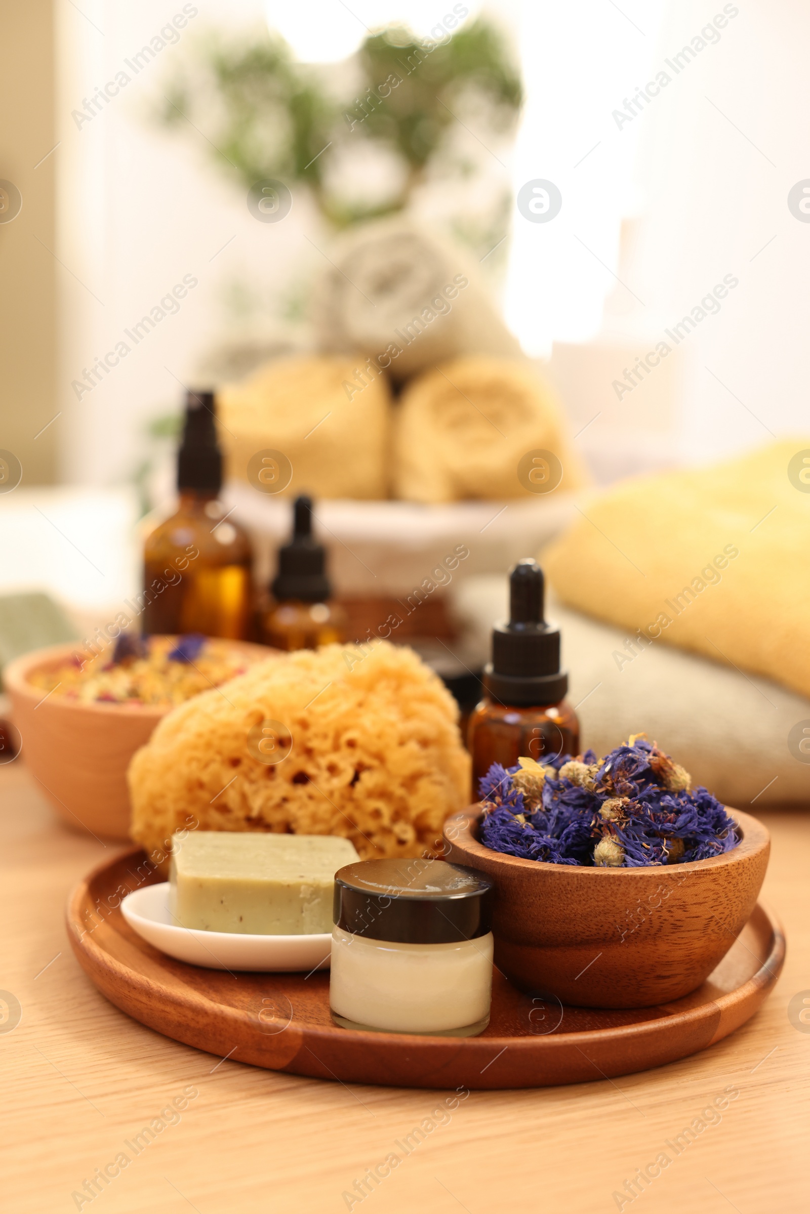 Photo of Dry flowers, loofah, soap bar, bottle of essential oil and jar with cream on wooden table indoors. Spa time