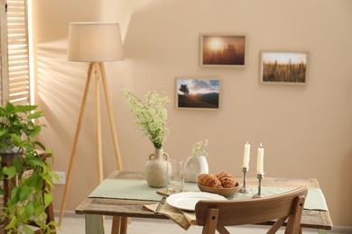 Photo of Clean tableware, candlesticks, flowers and fresh pastries on table in stylish dining room