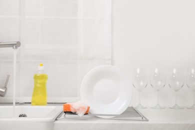 Photo of Drying rack with clean plate and soapy sponge in stylish kitchen