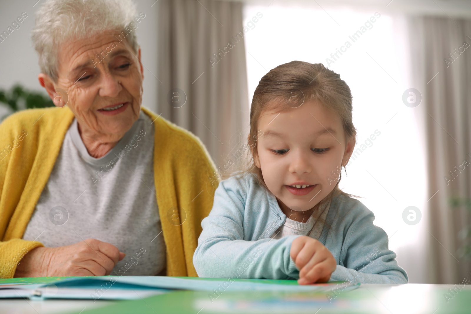 Photo of Cute girl and her grandmother reading book at home