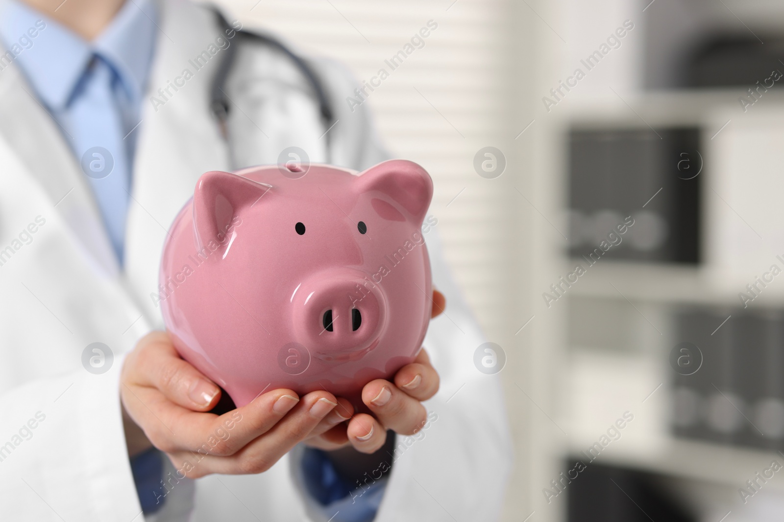 Photo of Doctor with pink piggy bank indoors, closeup. Space for text