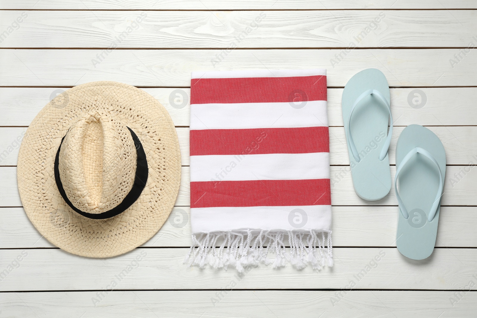 Photo of Beach towel, flip flops and straw hat on white wooden background, flat lay