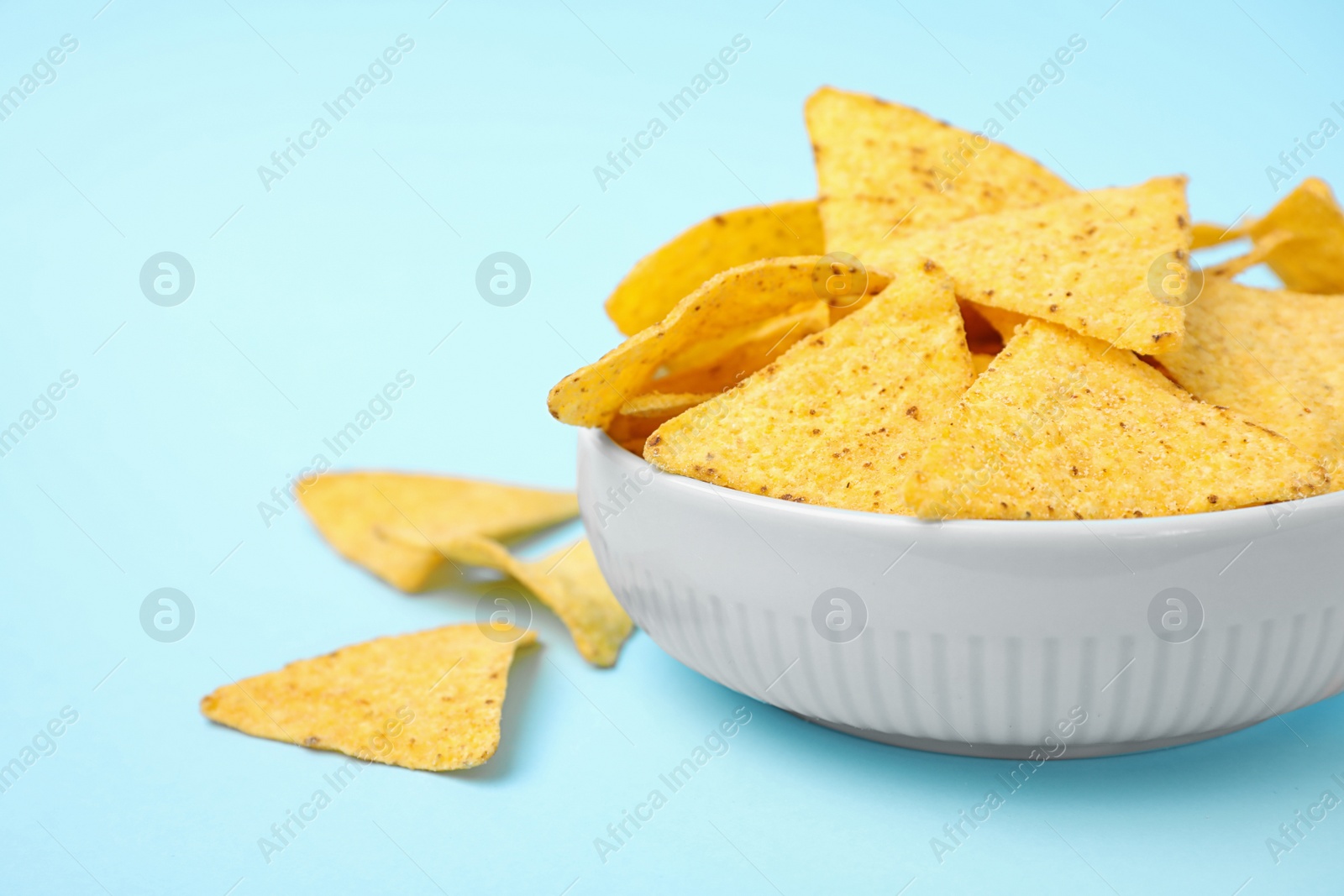 Photo of Bowl with tasty Mexican nachos chips on light blue background, space for text