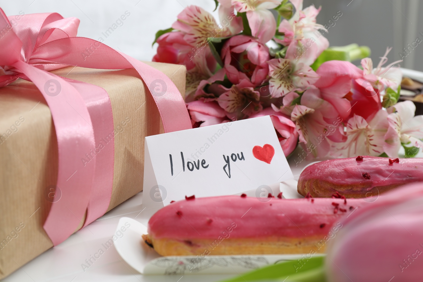 Photo of Tasty breakfast served in bed. Delicious eclairs, flowers, gift box and card with phrase I Love You on tray, closeup