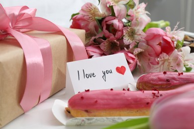 Photo of Tasty breakfast served in bed. Delicious eclairs, flowers, gift box and card with phrase I Love You on tray, closeup