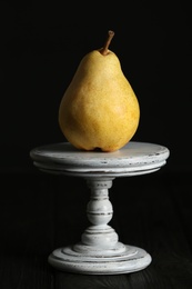 Stand with fresh ripe pear on table against dark background