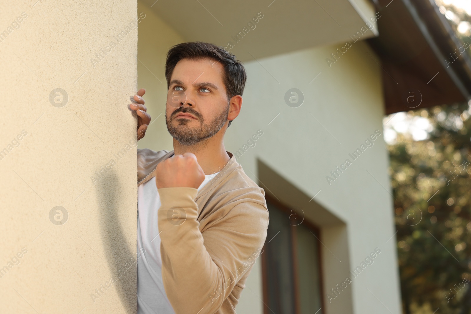 Photo of Angry man showing fist near house. Annoying neighbour