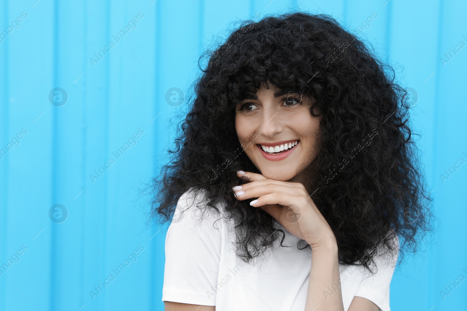 Photo of Portrait of beautiful woman near light blue wall. Attractive lady smiling and posing for camera. Space for text