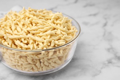 Photo of Uncooked trofie pasta in bowl on white marble table, closeup. Space for text