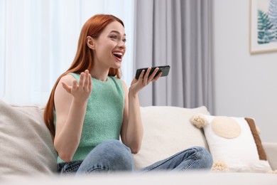 Photo of Happy woman sending voice message via smartphone on couch at home. Space for text