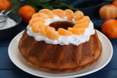 Photo of Homemade yogurt cake with tangerines and cream on blue wooden table, closeup