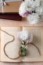 Photo of Book with chrysanthemum flowers as bookmark on beige textured background, flat lay