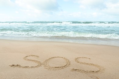 Photo of Message SOS drawn on sand near wavy sea