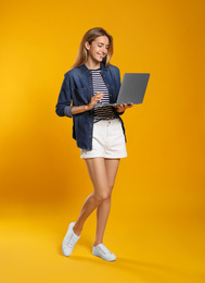 Full length portrait of young woman with modern laptop on yellow background