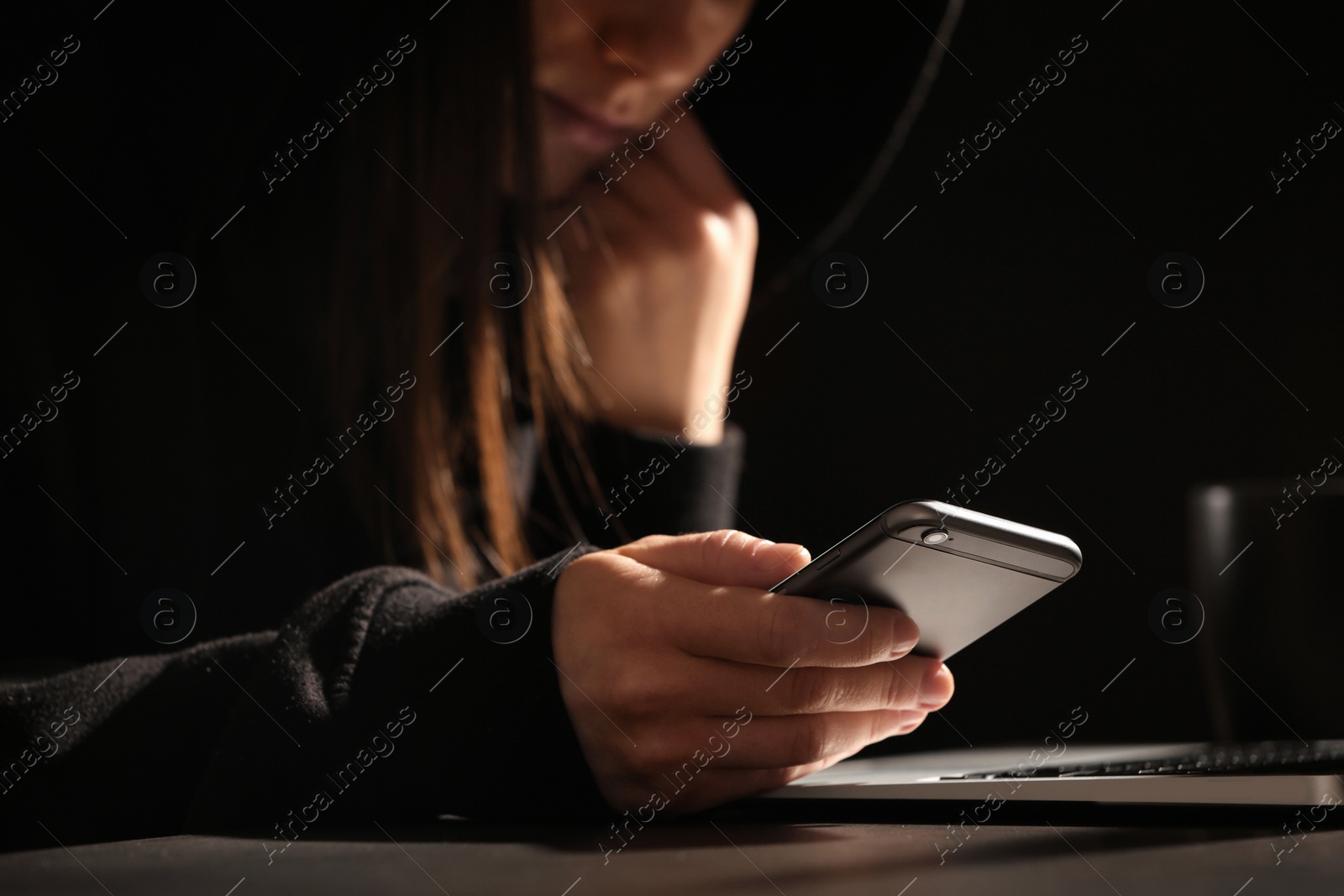 Photo of Woman using smartphone at table with laptop in darkness, closeup. Loneliness concept