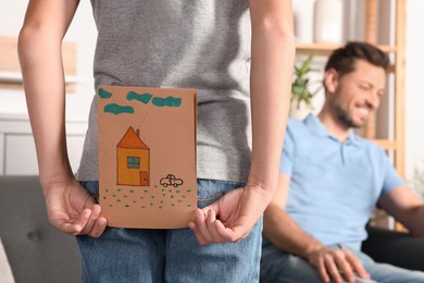 Photo of Boy hiding greeting card for his father behind back at home