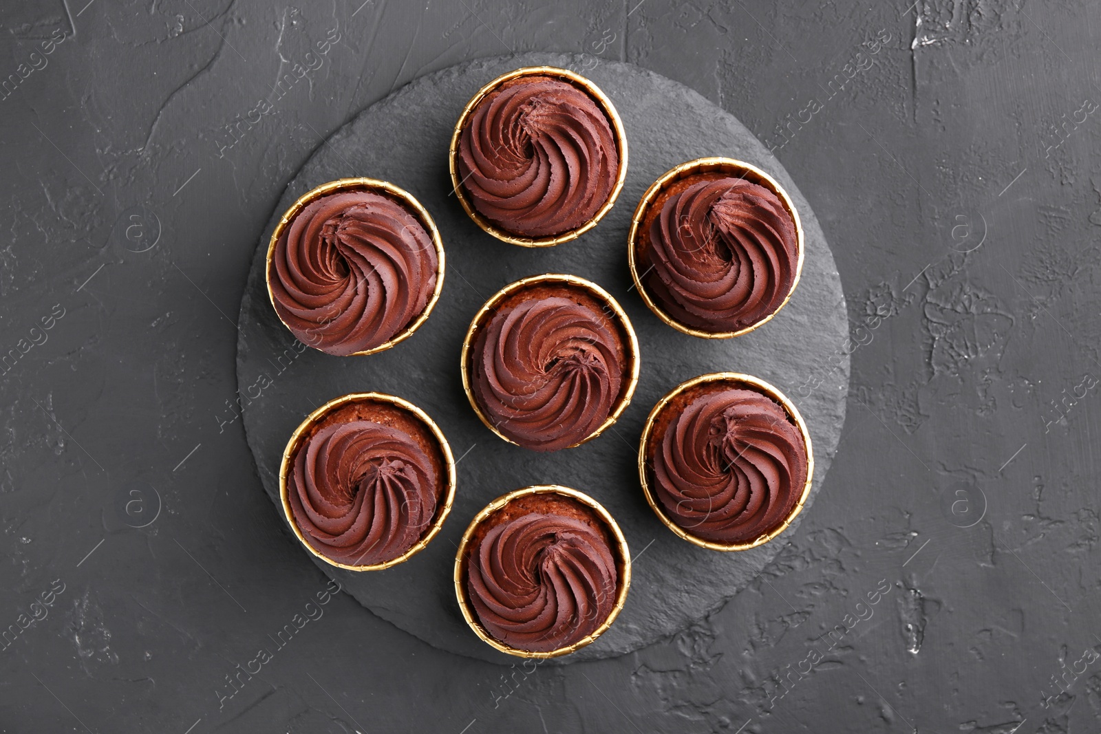 Photo of Delicious chocolate cupcakes on black textured table, top view