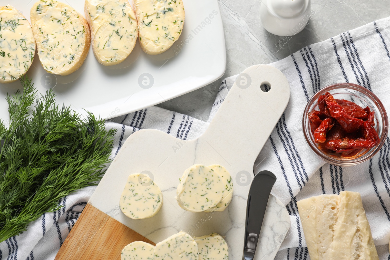 Photo of Tasty butter with dill, chili peppers, bread and knife on grey marble table, top view