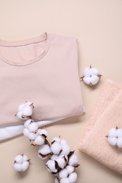 Photo of Cotton branch with fluffy flowers, t-shirts and terry towel on beige background, flat lay