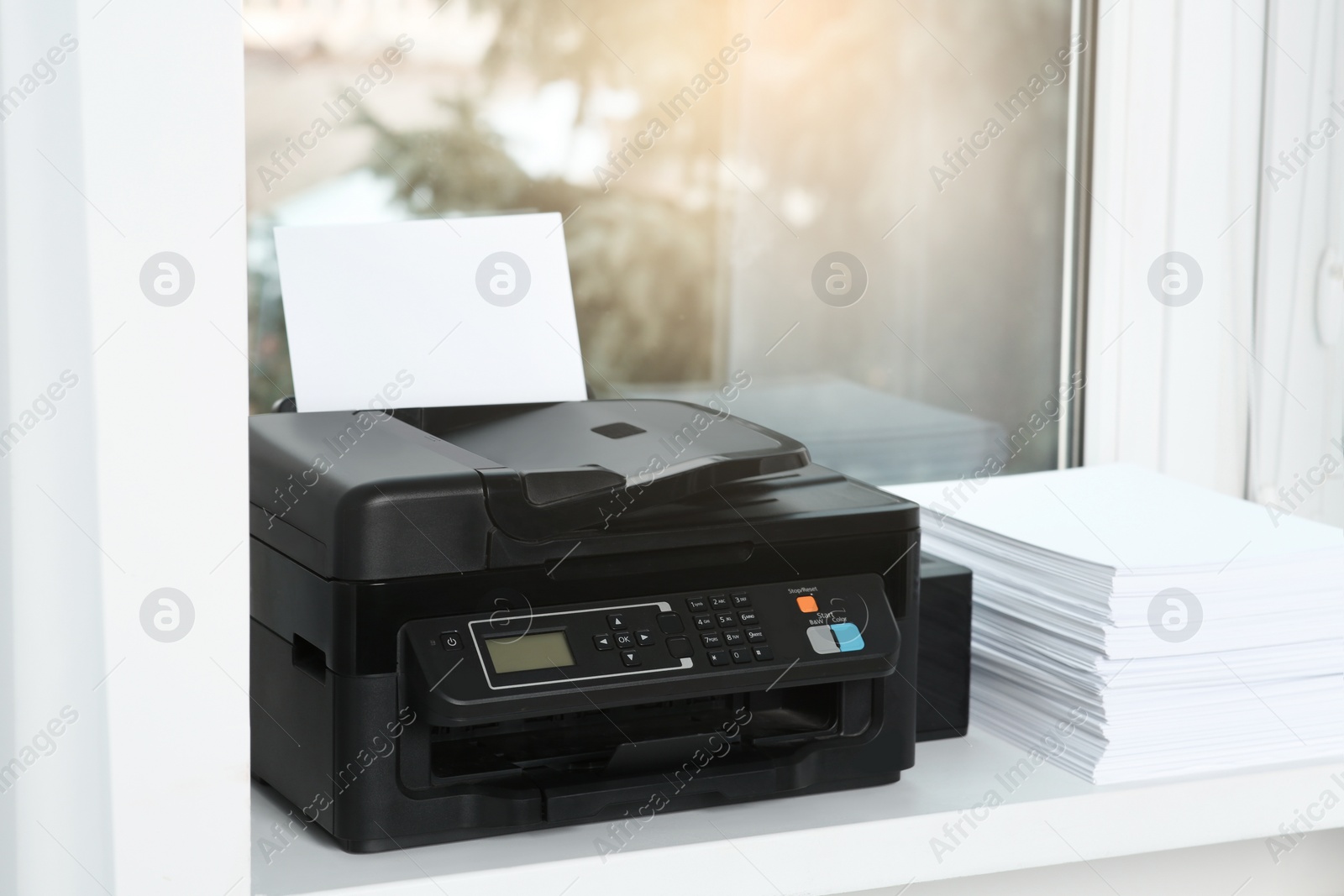 Photo of Modern printer and stack of paper on window sill indoors