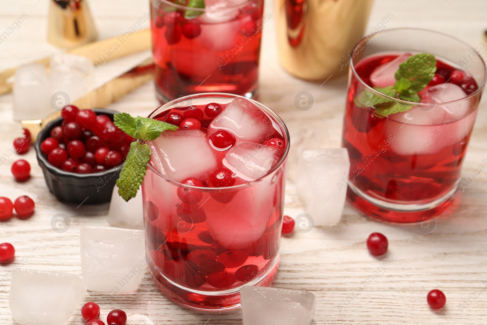 Photo of Tasty cranberry cocktail with ice cubes and mint in glasses on wooden table, closeup