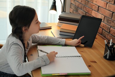 Photo of Little girl doing homework with modern tablet at home, focus on hand