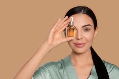 Young woman with bottle of essential oil on beige background. Space for text