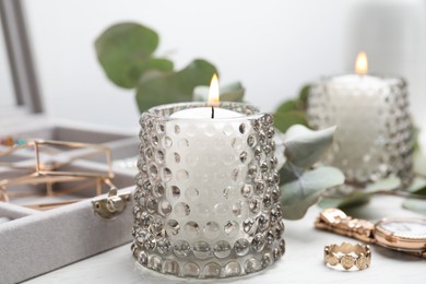 Photo of Burning candle and jewelry box with beautiful bijouterie on white wooden table, closeup