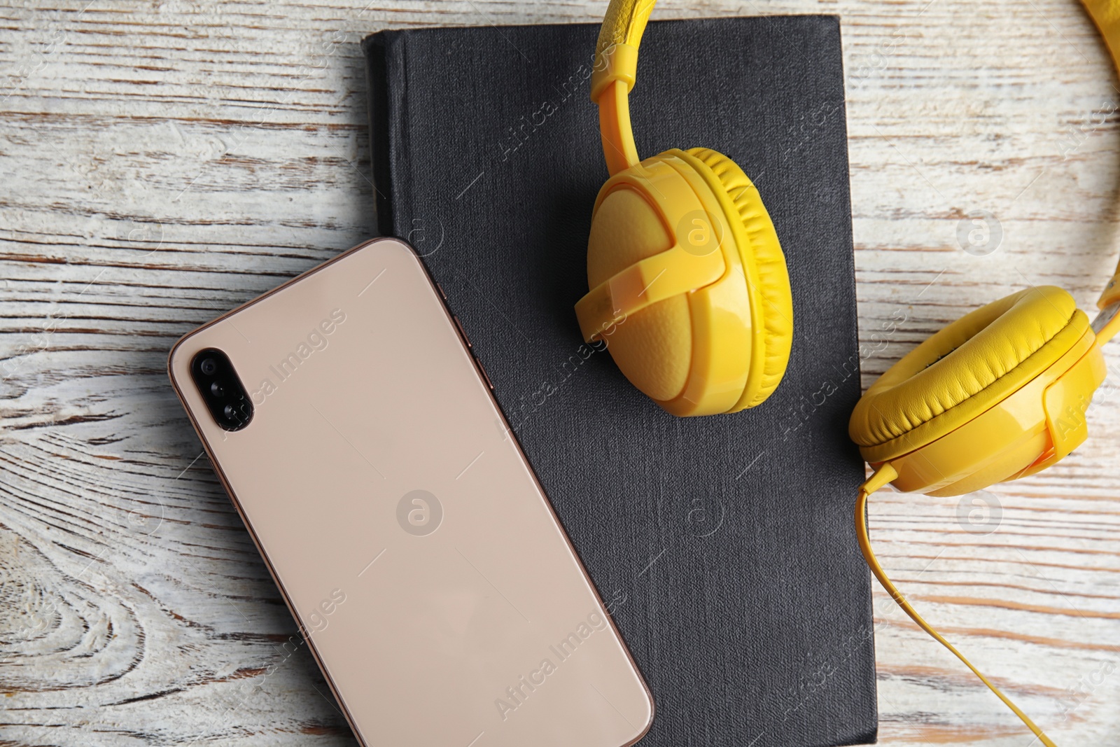 Photo of Book, modern headphones and smartphone on white wooden table, flat lay