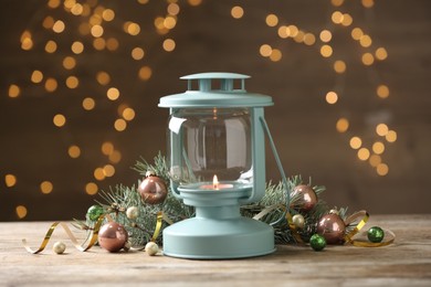 Photo of Lantern and Christmas decor on wooden table against blurred festive lights. Winter holiday