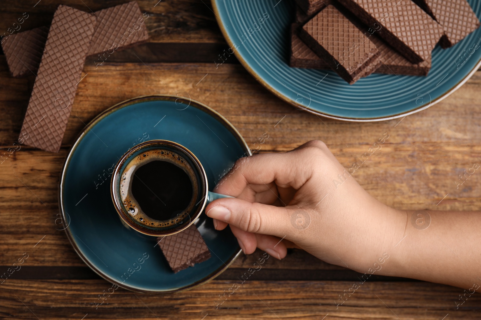 Photo of Woman having breakfast with cup of delicious coffee and wafers at wooden table, top view