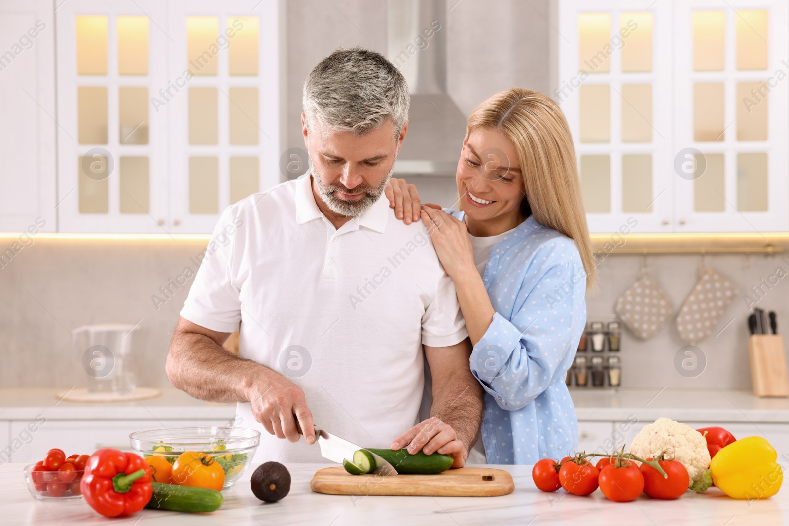 Photo of Happy affectionate couple cooking together at white table in kitchen