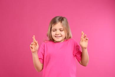 Photo of Cute little girl with crossed fingers on pink background