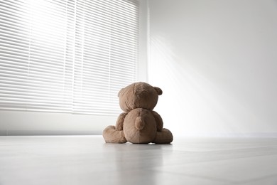 Photo of Cute lonely teddy bear on floor in empty room, back view