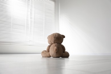 Cute lonely teddy bear on floor in empty room, back view