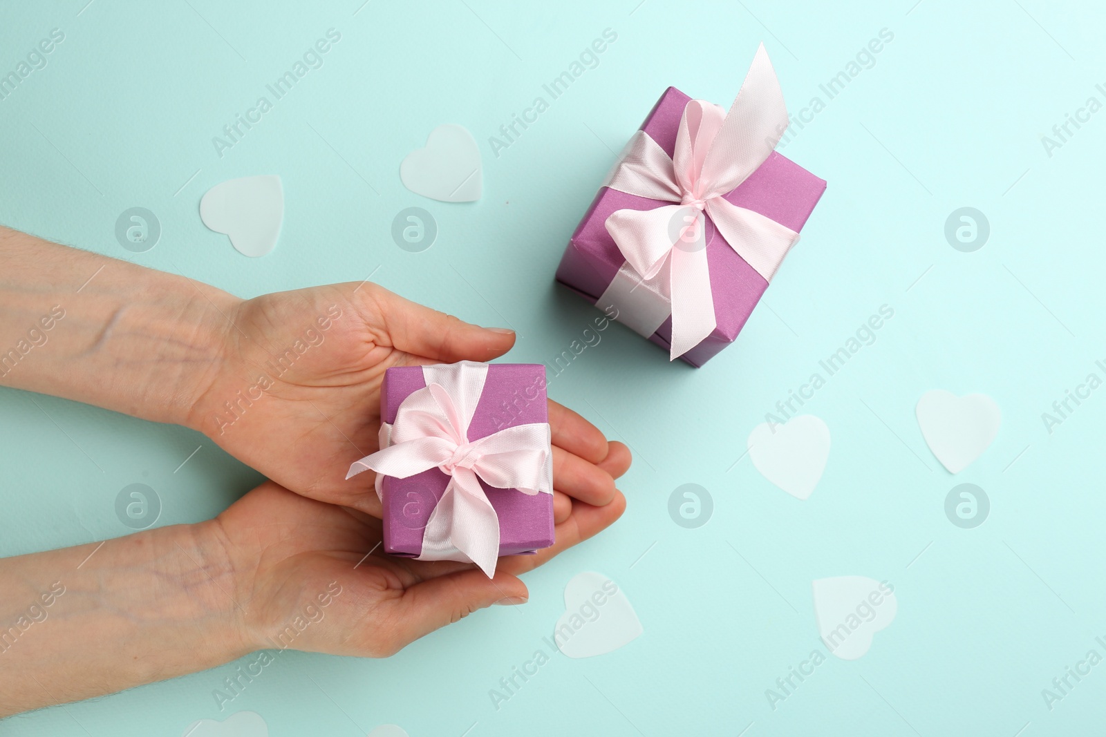 Photo of Woman holding gift box on turquoise background, top view. Valentine's Day celebration